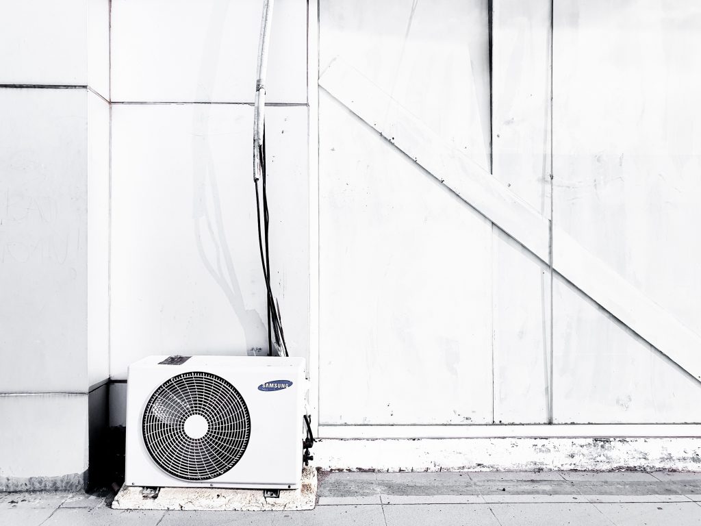 HVAC unit against a white wall, emphasizing the importance of regular HVAC inspections for system efficiency and maintenance.