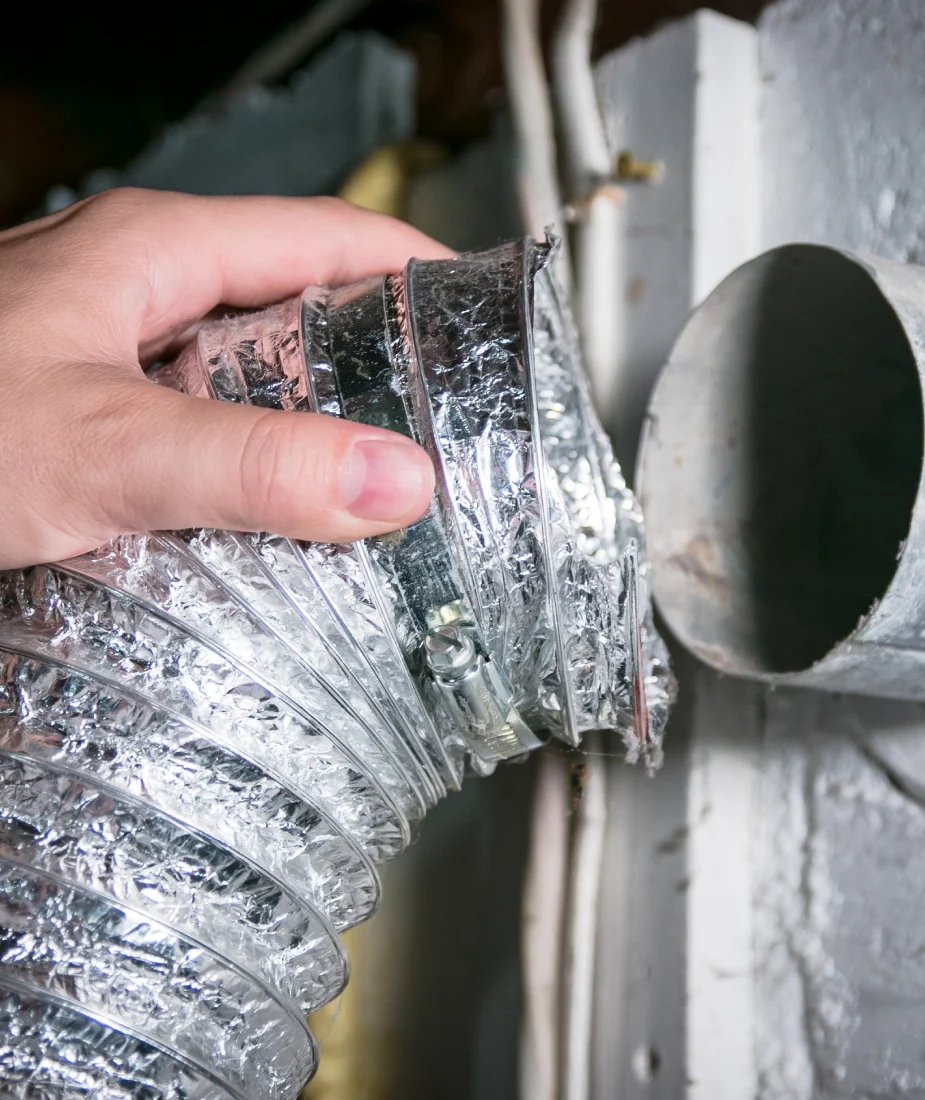 Hand holding flexible aluminum dryer vent duct, connecting to wall vent, illustrating dryer vent cleaning services in Sacramento for improved safety and efficiency.